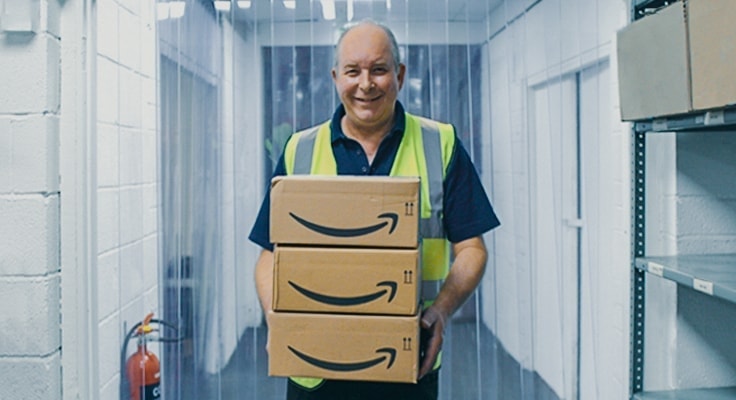 The Storage Place employee standing in a warehouse holding three boxes with Amazon Prime logo